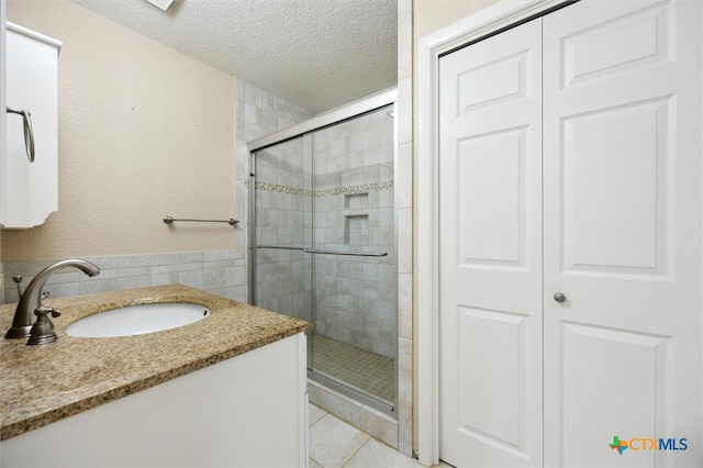 bathroom with a shower with door, tile patterned flooring, a textured ceiling, vanity, and tile walls