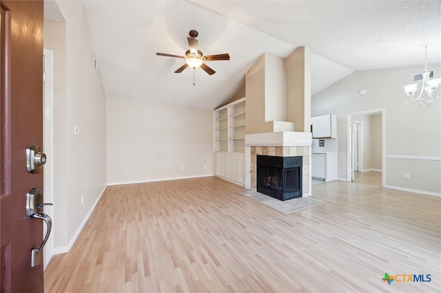 unfurnished living room with light wood-type flooring, a textured ceiling, a tiled fireplace, lofted ceiling, and ceiling fan with notable chandelier