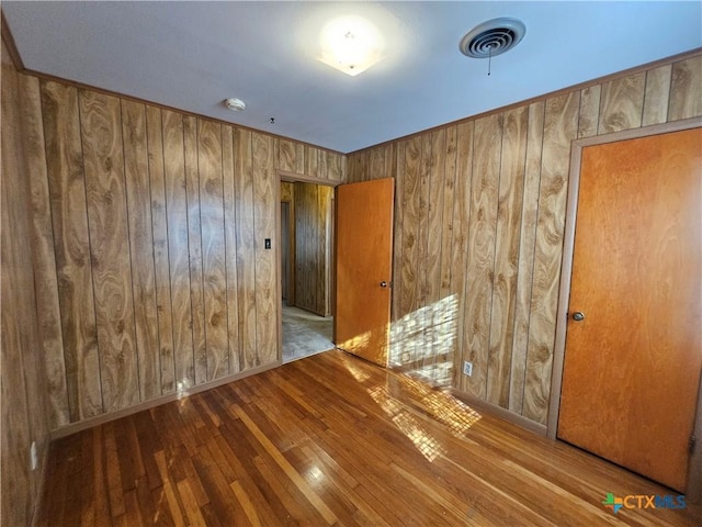 spare room with hardwood / wood-style floors, visible vents, and wood walls