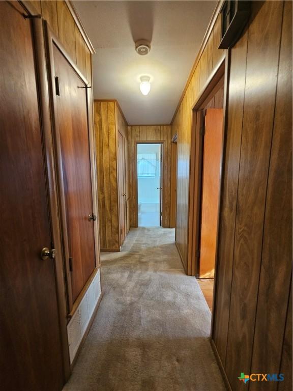 hallway featuring wooden walls, visible vents, and light carpet