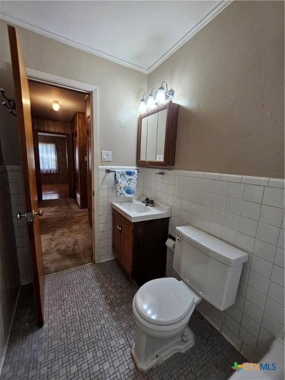 bathroom with tile walls, toilet, ornamental molding, wainscoting, and vanity