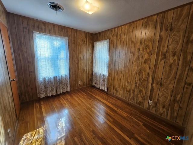 unfurnished room with visible vents, wooden walls, and hardwood / wood-style flooring