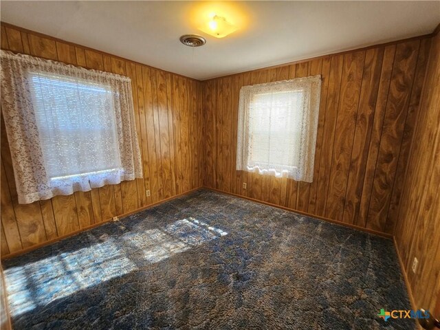 unfurnished room featuring wooden walls, carpet flooring, and visible vents