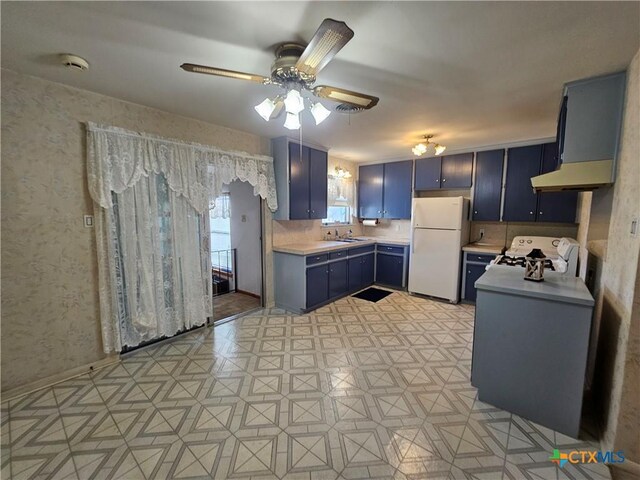 kitchen featuring wallpapered walls, blue cabinetry, freestanding refrigerator, a sink, and light countertops