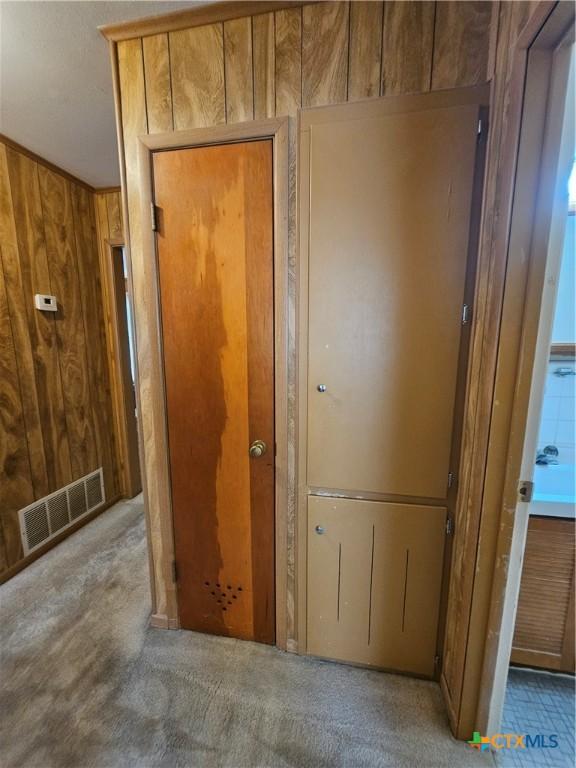 hallway featuring visible vents, wood walls, and carpet flooring