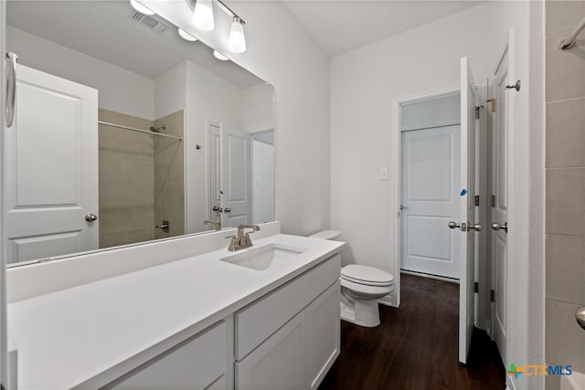 bathroom with wood-type flooring, vanity, toilet, and a tile shower