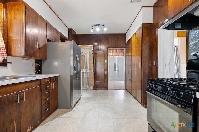 215 Taylor Rd, Elgin, TX 78621 - kitchen with wall chimney range hood, stainless steel refrigerator with ice dispenser, light countertops, black gas range oven, and wooden walls