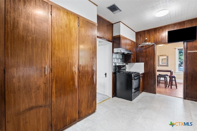 215 Taylor Rd, Elgin, TX 78621 - kitchen featuring visible vents, black gas stove, wooden walls, light floors, and under cabinet range hood