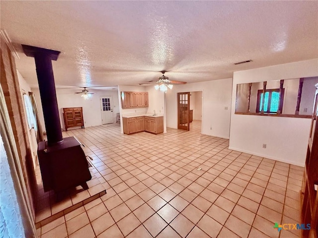 unfurnished living room featuring a wood stove, light tile patterned floors, and a textured ceiling