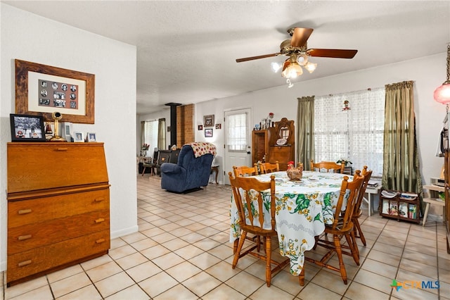 dining area with a wood stove, ceiling fan, light tile patterned flooring, and a textured ceiling