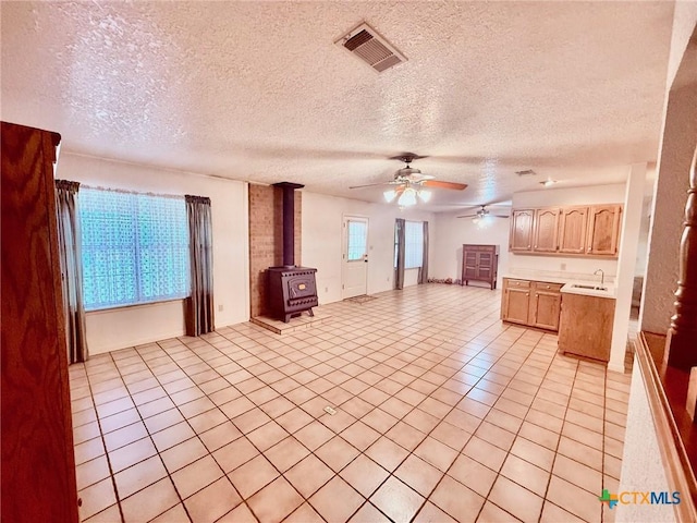 unfurnished living room featuring a wood stove, ceiling fan, sink, a textured ceiling, and light tile patterned floors