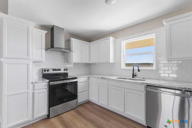 kitchen with a sink, stainless steel appliances, light wood-style floors, white cabinetry, and wall chimney exhaust hood