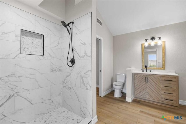 bathroom featuring visible vents, toilet, wood finished floors, tiled shower, and vanity