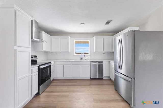 kitchen featuring visible vents, light wood-style flooring, appliances with stainless steel finishes, wall chimney exhaust hood, and light countertops