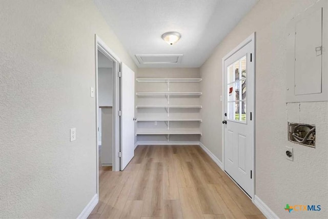 corridor featuring attic access, electric panel, baseboards, and light wood-type flooring