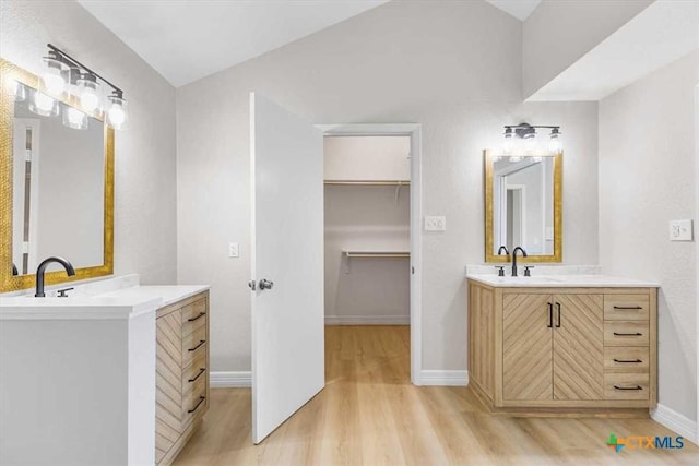 bathroom with a spacious closet, two vanities, wood finished floors, and a sink