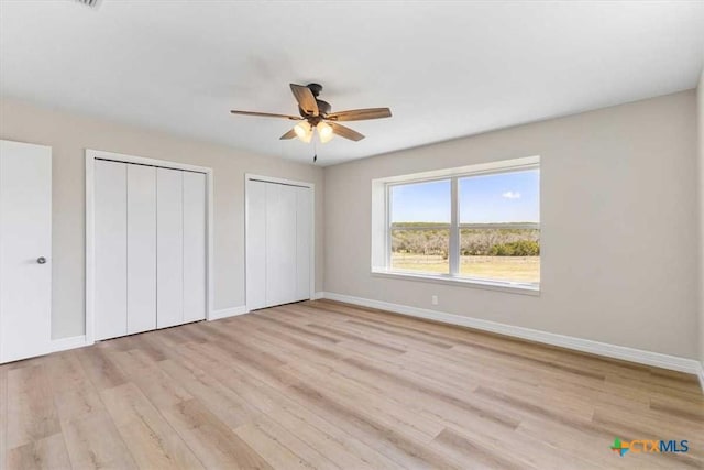 unfurnished bedroom with light wood finished floors, baseboards, and two closets