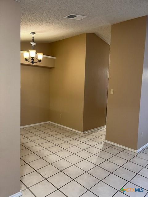 tiled spare room with a textured ceiling and a chandelier