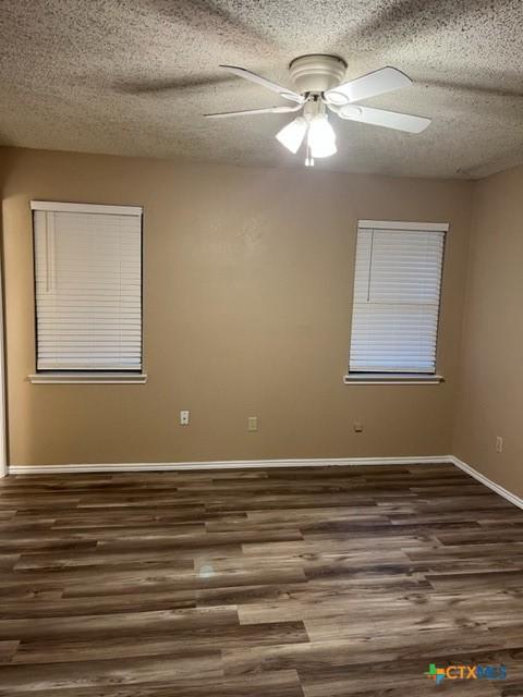 empty room with a textured ceiling, ceiling fan, and dark hardwood / wood-style floors