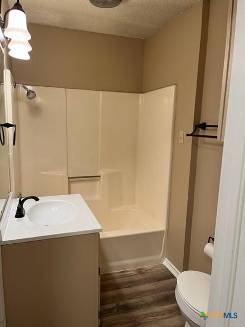 full bathroom featuring wood-type flooring, a textured ceiling, toilet, vanity, and shower / bathtub combination