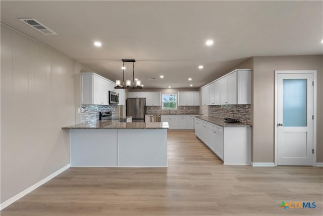 kitchen featuring kitchen peninsula, stainless steel appliances, light hardwood / wood-style flooring, white cabinetry, and hanging light fixtures