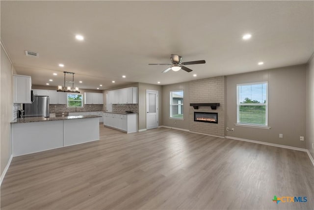 kitchen with light wood-type flooring, decorative light fixtures, white cabinetry, and stainless steel refrigerator