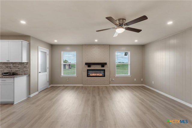 unfurnished living room featuring ceiling fan, plenty of natural light, light hardwood / wood-style flooring, and a brick fireplace