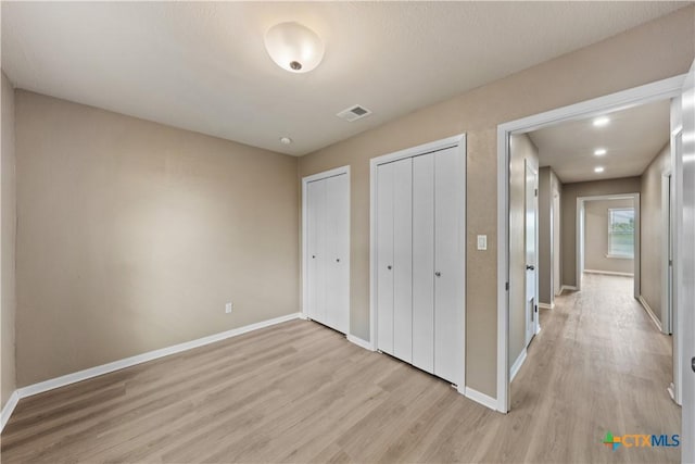 unfurnished bedroom with light hardwood / wood-style floors and two closets