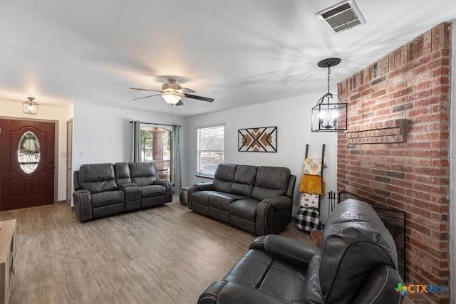 living room featuring a fireplace, wood-type flooring, and ceiling fan with notable chandelier