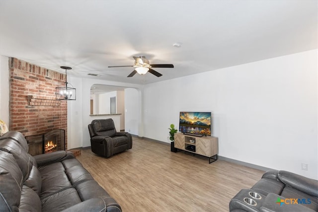 living room with a brick fireplace, ceiling fan, and light wood-type flooring