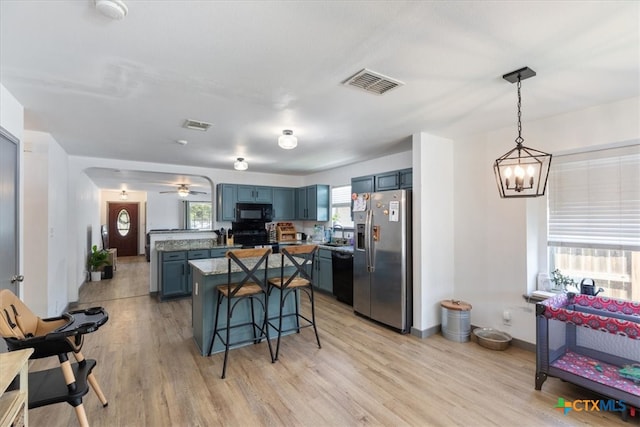 kitchen featuring black appliances, blue cabinetry, decorative light fixtures, a kitchen bar, and light hardwood / wood-style floors