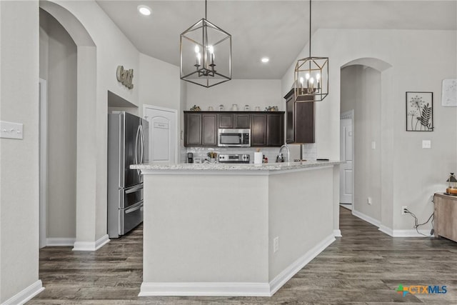 kitchen featuring light stone countertops, dark hardwood / wood-style floors, decorative light fixtures, dark brown cabinets, and appliances with stainless steel finishes