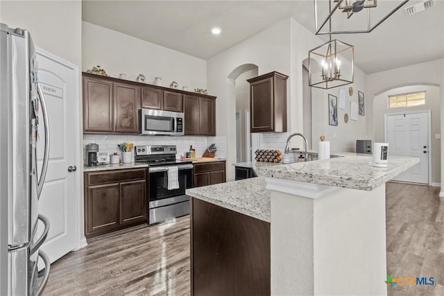 kitchen with light stone counters, stainless steel appliances, decorative light fixtures, an inviting chandelier, and light hardwood / wood-style flooring