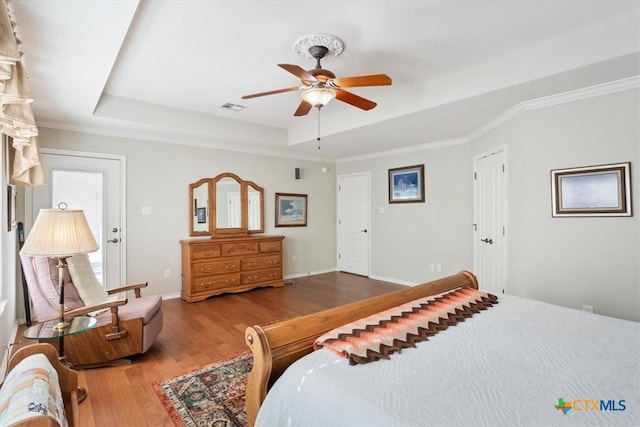 bedroom with a tray ceiling, ceiling fan, wood-type flooring, and ornamental molding