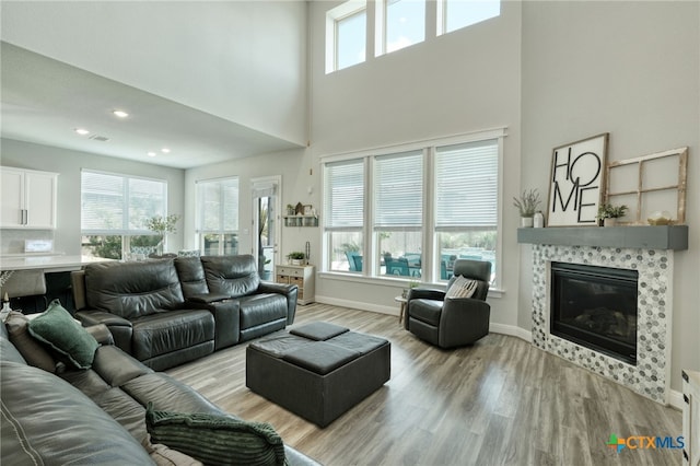 living room featuring a tile fireplace, light wood finished floors, baseboards, a towering ceiling, and visible vents