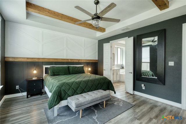 bedroom featuring beamed ceiling, a decorative wall, wood finished floors, and visible vents