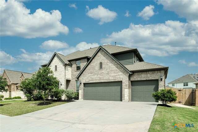 french country home featuring a garage, fence, concrete driveway, and stone siding