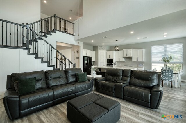 living area with stairway, a high ceiling, recessed lighting, and light wood finished floors