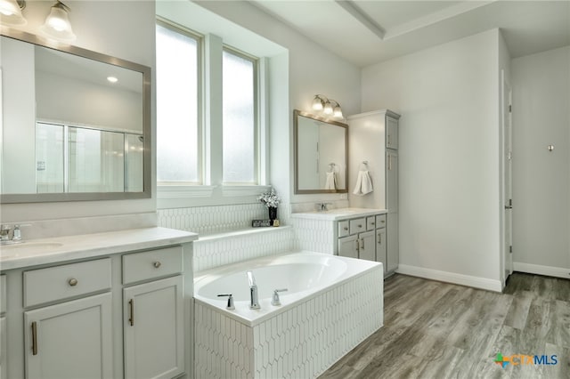 full bathroom featuring a sink, two vanities, wood finished floors, a bath, and a stall shower