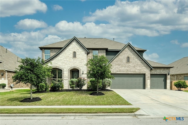 french country style house with roof with shingles, an attached garage, stone siding, a front yard, and driveway