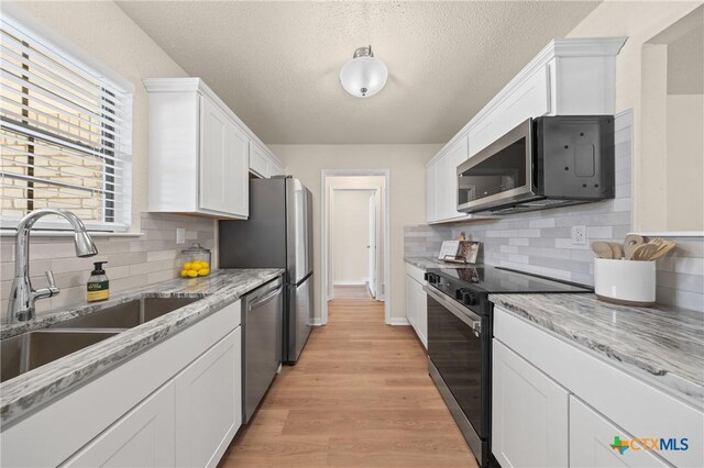 116 Spur Dr, Copperas Cove, TX 76522 - kitchen featuring stainless steel appliances, white cabinetry, light wood-style floors, tasteful backsplash, and a textured ceiling
