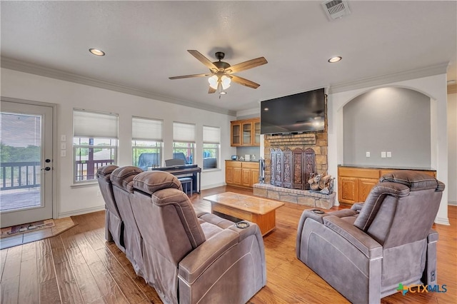 living room featuring crown molding, light wood-style flooring, a fireplace with raised hearth, a ceiling fan, and recessed lighting