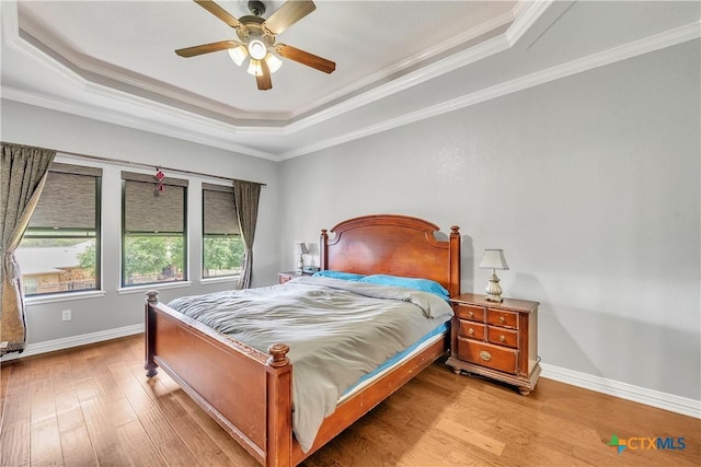 bedroom featuring a raised ceiling, wood finished floors, baseboards, and crown molding