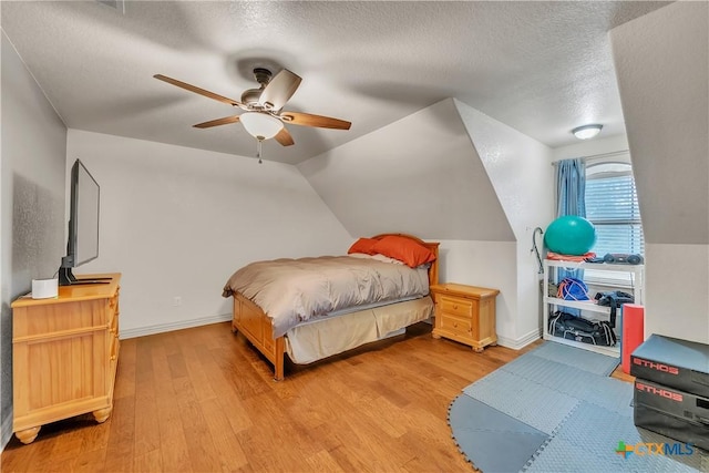 bedroom with light wood-type flooring, a textured ceiling, ceiling fan, lofted ceiling, and baseboards
