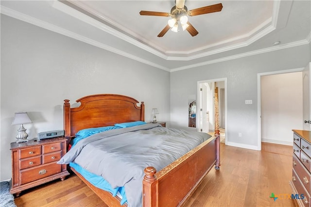 bedroom featuring a raised ceiling, light wood finished floors, crown molding, ceiling fan, and baseboards