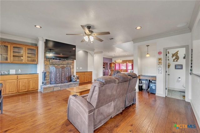 living area featuring ceiling fan, wood-type flooring, ornamental molding, a fireplace, and recessed lighting