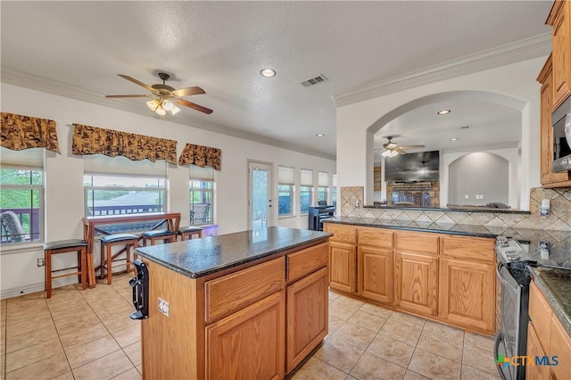 kitchen featuring ceiling fan, stainless steel range with electric cooktop, tasteful backsplash, light tile patterned floors, and a kitchen island