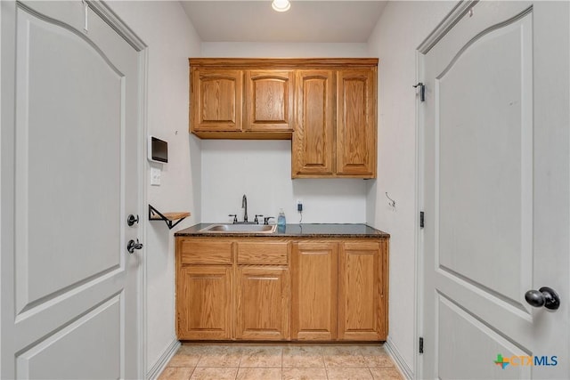 kitchen with a sink, dark countertops, brown cabinetry, baseboards, and light tile patterned floors