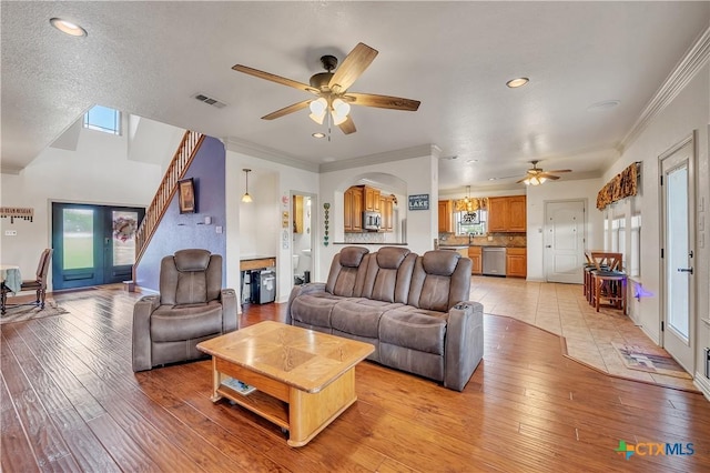living room featuring a ceiling fan, light wood-style floors, arched walkways, ornamental molding, and recessed lighting