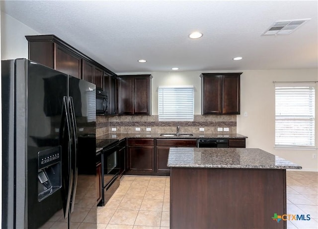 1321 Cozy Creek Dr, Temple, TX 76502 - kitchen with black appliances, light tile patterned floors, dark stone counters, dark brown cabinetry, and a kitchen island